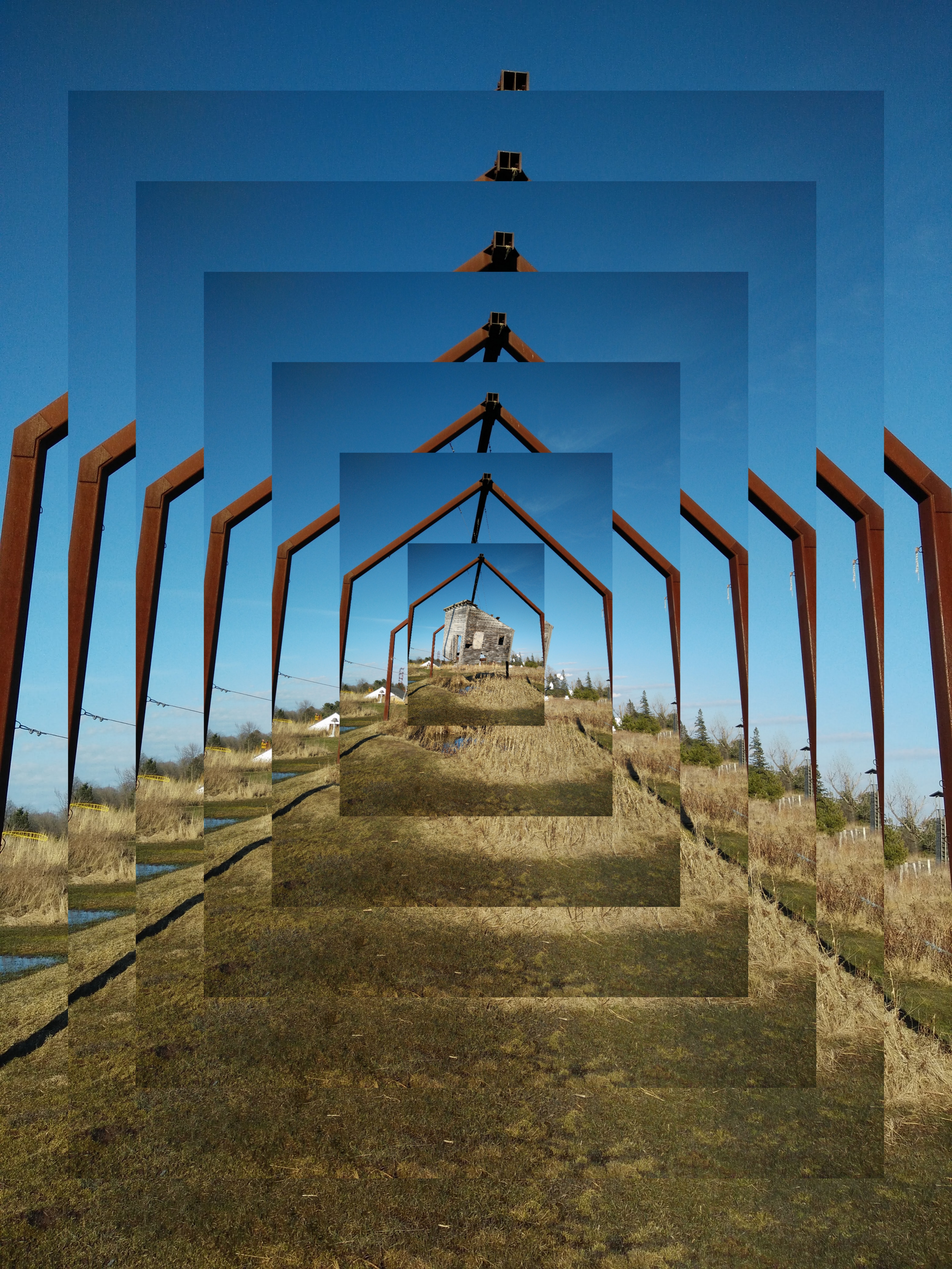 A sculpture of a large, decaying shed, suspended above the ground by a series of ropes woven through the shed and attached to large metal beams. The photo has been modified with image editing software to show the original image in the inner most rectangle at the center of the edited image, with six additional rectangle &rsquo;layers&rsquo; stretching the image, particularly it&rsquo;s rusting red legs, and eminating out in increasing sizes from the center of the photograph.
