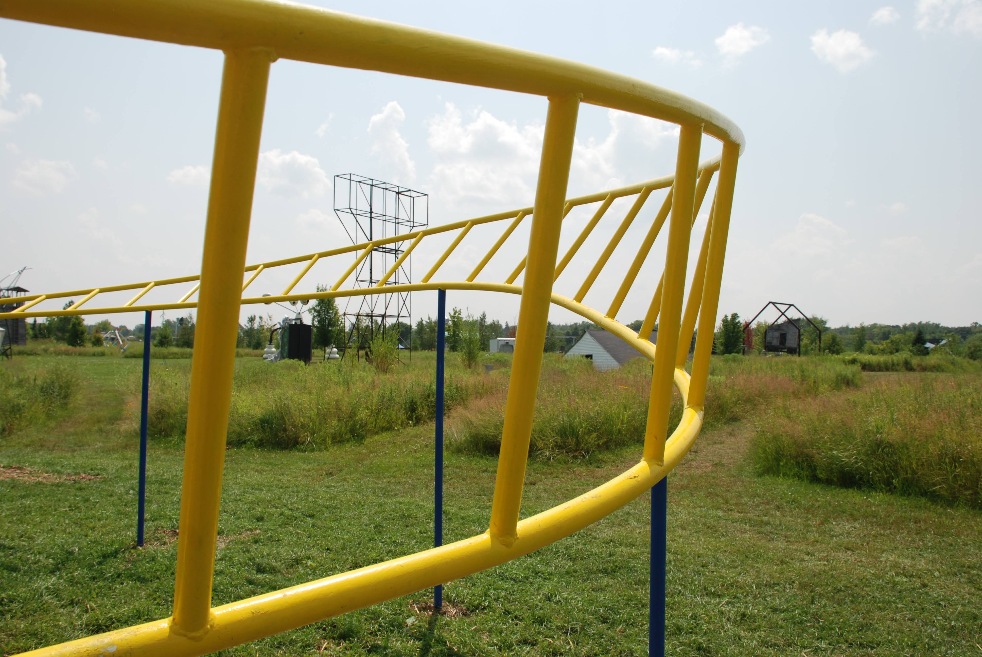 A steel sculpture with blue support poles and yellow twisting sets of bars, similar to something you’d encounter on a children’s playground. Which makes sense when the purpose of the sculpture is to be interactive and be a “playful twist on familiar pastimes and amusements.”